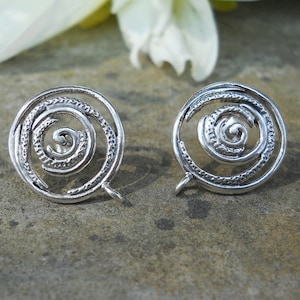 May include: A pair of silver earrings with a spiral design. The earrings are round and have a textured surface.