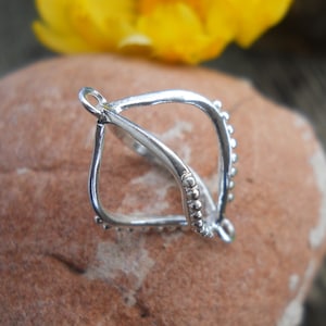 May include: Silver pendant with a geometric design and a beaded edge. The pendant is shaped like a teardrop and has a loop at the top for attaching a chain.