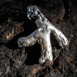 May include: A silver-colored, abstract, three-dimensional sculpture of a person with a rough, textured surface.