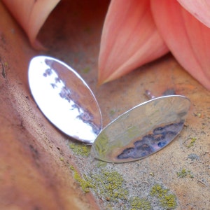 May include: A pair of silver earrings with a hammered finish. The earrings are oval shaped and have a smooth, reflective surface.