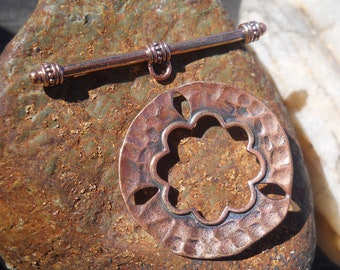 May include: A copper toggle clasp with a hammered finish and a decorative flower cutout. The clasp is attached to a copper bar with decorative beads.