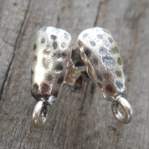 May include: A pair of silver stud earrings with a hammered texture. The earrings have a simple, minimalist design.
