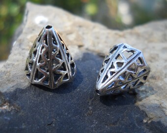 May include: Two silver metal cone-shaped beads with an intricate geometric design. The beads are made of a filigree pattern and have a shiny finish.