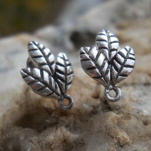 May include: Two silver-colored leaf-shaped earring charms. Each charm features three detailed leaves with visible veins. The charms have a small loop at the base for attachment, perfect for jewelry making.