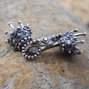 May include: Silver-toned metal clasp with a crown design on each end. The clasp is detailed with small beads and a geometric pattern.