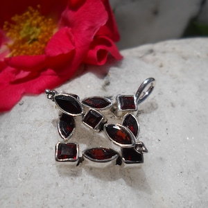 May include: A silver pendant with a square design featuring multiple red garnet stones.