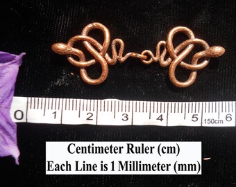 May include: A copper-colored snake clasp measuring approximately 5 cm in length. The clasp is made of two intertwined snakes with detailed scales. The clasp is shown against a black background with a ruler for scale.