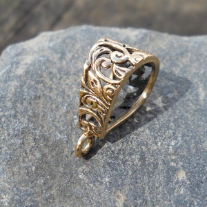 May include: Gold-toned metal pendant bail with an intricate, ornate design. The bail is shaped like a teardrop and has a loop at the top for attaching a chain.