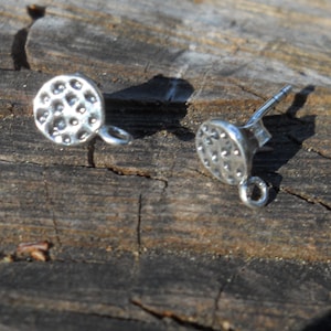 May include: A pair of silver earring posts with a textured round disc and a small loop on each post.