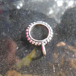 Può includere: Anello in metallo argentato con un bordo perlato e un piccolo anello in basso. L'anello è progettato per essere utilizzato come connettore per gioielli o altri oggetti artigianali.