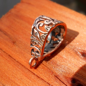 Puede incluir: Un cierre de colgante plateado con un diseño intrincado y ornamentado. El cierre tiene forma de lágrima y tiene un bucle en la parte superior para sujetar un colgante.