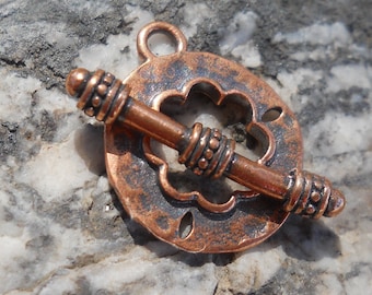 May include: A copper-toned metal clasp with a decorative flower design. The clasp has a round shape and a bar that goes through the center. The clasp is designed for jewelry making.