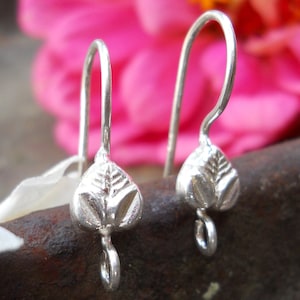 May include: A pair of silver earring hooks with a leaf design. The hooks are made of metal and have a shiny finish.