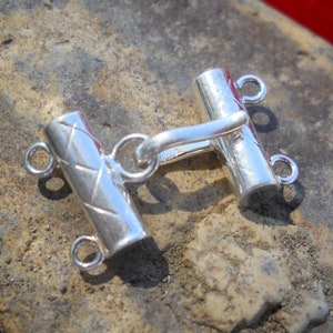 May include: Silver toggle clasp with two loops on each end. The clasp has a textured design.