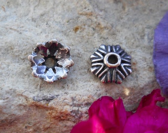May include: Two silver metal bead caps with a decorative design. One cap has a starburst design and the other has a flower design.