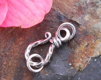 May include: Silver clasp with a twisted design. The clasp is made of metal and has a polished finish.