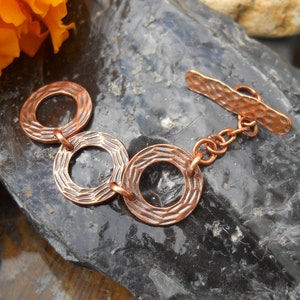 May include: A copper bracelet with three hammered circles connected by a chain and a hammered clasp.