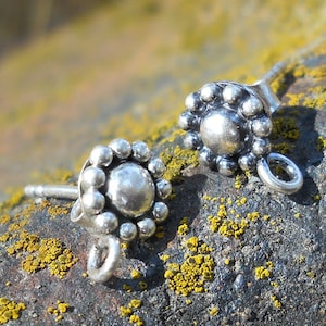 May include: Two silver earring findings with a round, beaded design and a small loop for attaching a charm or pendant.