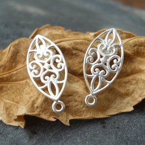 May include: A pair of silver filigree earrings with a leaf-shaped design. The earrings have a delicate, intricate pattern and a small loop at the bottom.