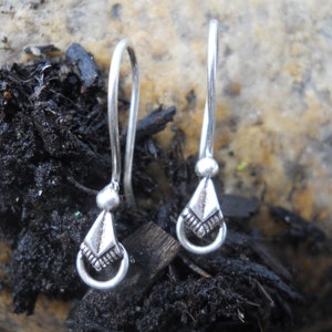 May include: A pair of silver dangle earrings with a geometric design. The earrings are made of a thin silver wire and have a small, triangular pendant at the bottom.