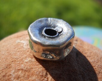 May include: A silver metal bead with a hole in the center. The bead has a rough, textured surface.