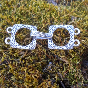 May include: Silver clasp with a geometric design. The clasp has two loops on each side and a decorative center piece.