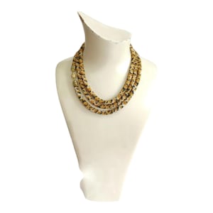 May include: A multi-strand necklace made of small, black, white, and gold beads. The necklace is layered and has a chunky, textured look.