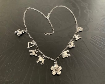 May include: Silver necklace with a variety of charms, such as dog shapes, a heart, a flower, and a rose. The necklace has a fine chain and an adjustable fastening. The charms are detailed, adding a whimsical element to the jewellery.