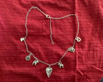 May include: A silver chain necklace with multiple charms, including hearts, roses, and small animal figures. The necklace is on a red background.