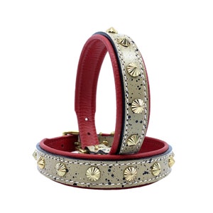 May include: Two leather bracelets. The outer band is tan with black speckles and gold-colored studs. The inner band is red. The bracelets are stacked on top of each other, with a gold-colored buckle.