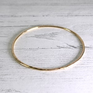 May include: A simple gold bangle bracelet with a hammered finish.