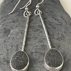 May include: A pair of silver dangle earrings with a hammered texture. Each earring features a smooth, gray, oval-shaped stone.