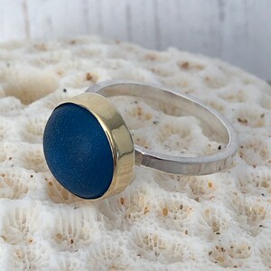 May include: A ring with a blue glass stone set in a gold band. The band is attached to a silver band.