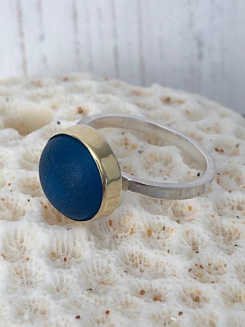 May include: A ring with a blue glass stone set in a gold band. The band is attached to a silver band.