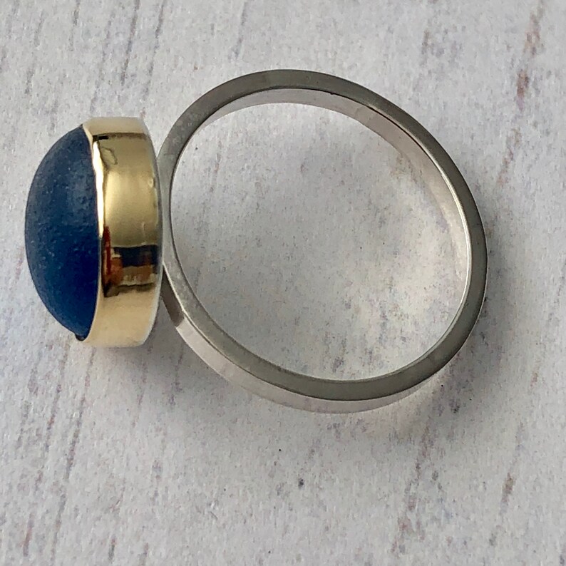 May include: A silver ring with a blue and gold cabochon gemstone. The ring is set on a white background.
