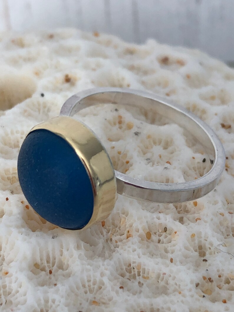 May include: A silver ring with a gold band and a blue glass stone.