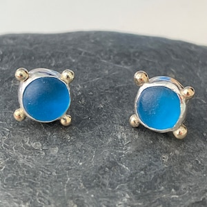 May include: A pair of silver stud earrings with a blue glass center and gold accents.