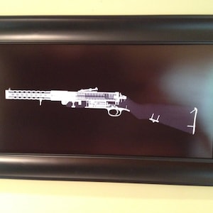 May include: Framed print featuring a white, detailed illustration of a machine gun against a dark background. The artwork is encased in a black frame, creating a striking contrast. The image is a detailed technical drawing of the weapon.