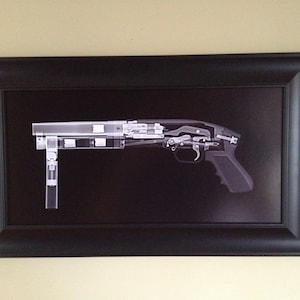 May include: A framed print of a shotgun's internal components, rendered in a grayscale X-ray style. The image is set against a black background within a black frame, showcasing the firearm's mechanics.