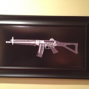 May include: Framed artwork featuring a detailed, x-ray style illustration of a firearm against a black background. The gun is rendered in shades of gray and white, with visible internal components. The artwork is encased in a black frame.