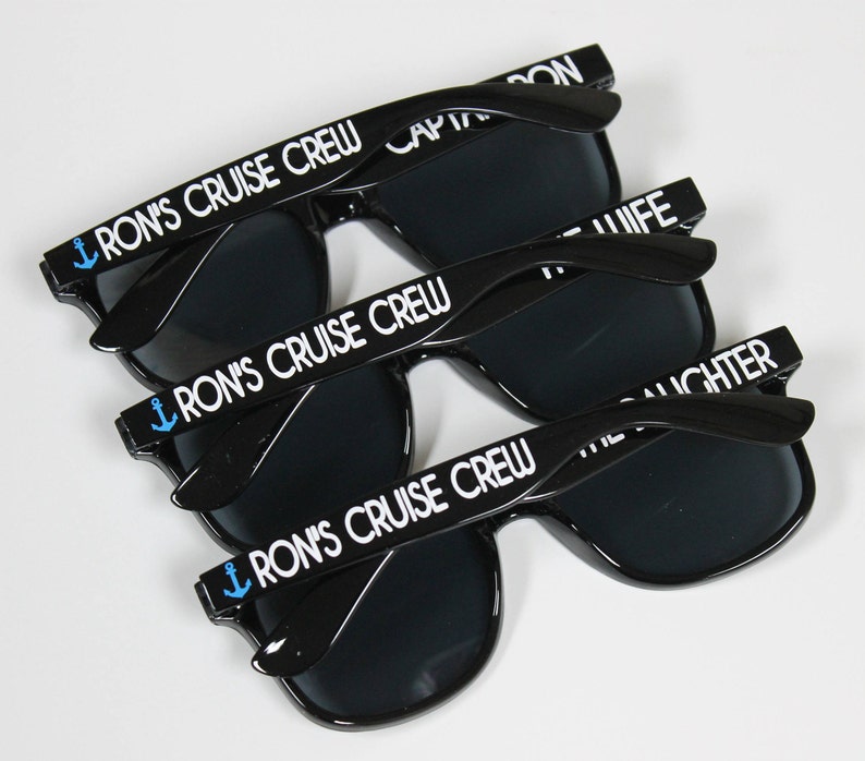 May include: Three pairs of black sunglasses with dark lenses. Each pair has a white anchor and the text "Ron's Cruise Crew" on the arms.