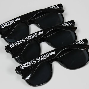 May include: Three black sunglasses with white text. The top pair says "Groom" with a mustache symbol. The middle and bottom pairs say "Groom's Squad" with a mustache symbol.