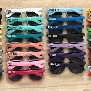 May include: A collection of 24 pairs of sunglasses with various colored frames and lenses. Each pair has a different color name printed on the frame, such as "Black", "White", "Powder Blue", "Yellow", "Orange", "Mint Green", "Sky Blue", "Aqua/Light Teal", "Royal Blue", "Lime Green", "Dark Teal", "Navy Blue", "Green", "Rose Gold", "Coral", "Lilac", "Red", "Silver", "Gray", "Blush Pink", "Purple", "Maroon", "Pink", "Dark Plum", "Hot Pink", and "Rainbow".
