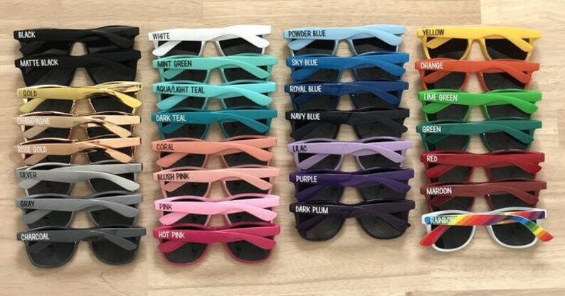 May include: A collection of 24 pairs of sunglasses with various colored frames and lenses. Each pair has a different color name printed on the frame, such as "Black", "White", "Powder Blue", "Yellow", "Orange", "Mint Green", "Sky Blue", "Aqua/Light Teal", "Royal Blue", "Lime Green", "Dark Teal", "Navy Blue", "Green", "Rose Gold", "Coral", "Lilac", "Red", "Silver", "Gray", "Blush Pink", "Purple", "Maroon", "Pink", "Dark Plum", "Hot Pink", and "Rainbow".