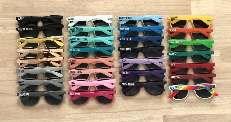 May include: A set of 24 colorful sunglasses with different colored frames and black lenses. Each pair has a different color name printed on the frame, such as black, white, powder blue, yellow, mint green, sky blue, orange, gold, aqua/light teal, royal blue, lime green, dark teal, navy blue, green, rose gold, coral, lilac, red, silver, blush pink, purple, maroon, charcoal, hot pink, and rainbow.