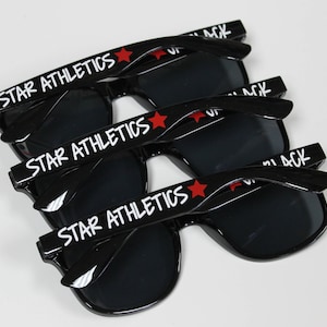 May include: Three black sunglasses with red stars and the words "STAR ATHLETICS" printed on the arms.