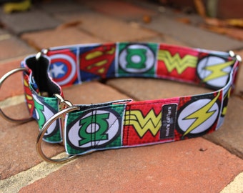 May include: A fabric dog collar featuring a repeating pattern of various superhero logos including the Green Lantern, Wonder Woman, Flash, Superman, and Captain America emblems. The collar includes two silver-toned metal D-rings and a small black tag.