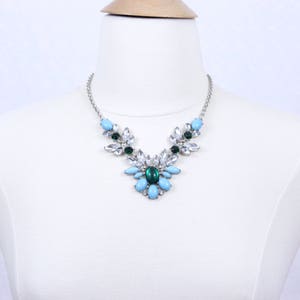 May include: A silver necklace with a cluster of light blue and green gemstones. The necklace features a floral design with a central light blue stone.