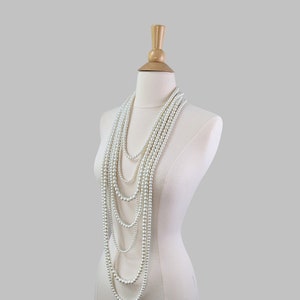 Puede incluir: Un collar de perlas blancas con múltiples hebras drapeado sobre un busto de maniquí blanco.