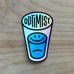 Puede incluir: Una pegatina holográfica con un vaso azul con una cara sonriente y la palabra "OPTIMIST" escrita en la parte superior.